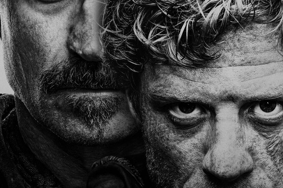 A black and white photograph shows two men standing with their faces very close together. They both have serious expressions on their faces and are staring down the lens of the camera. Across the bottom are the words KING & CONQUEROR