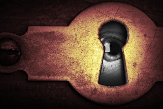 An eye looking through a dark keyhole.