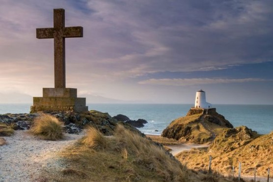 Twr Mawr Lighthouse and St Dwynwen's stone cross at sunrise on Llanddwyn Island on Anglesey.