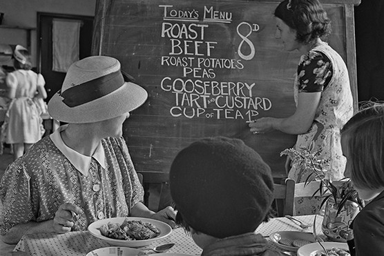 Diners watch a waitress chalk up the dishes offered on the day's menu at a British Restaurant in Gillingham, 1941. (Photo by Reuben Saidman/ Popperfoto via Getty Images)