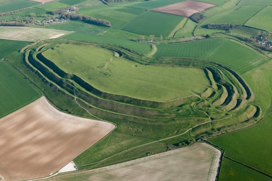 An aerial shot of a large expanse of green land with layered edges; the site of Maiden Castle hillfort