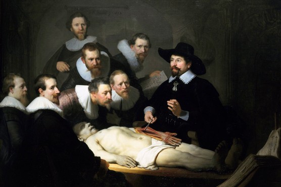 A group of men observe a body lying on a table.