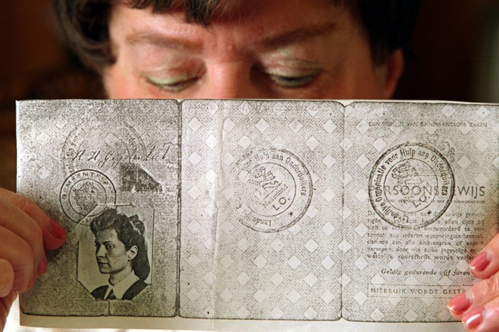 A Jewish woman holds a copy of fake papers enabling her to flee the Netherlands after the Nazi invasion: AI helps researchers search huge archives of testimonies by Holocaust survivors (Image by Getty Images) A woman holds up an old passport in front of her face. On the left page there is a black and white photo of a young girl
