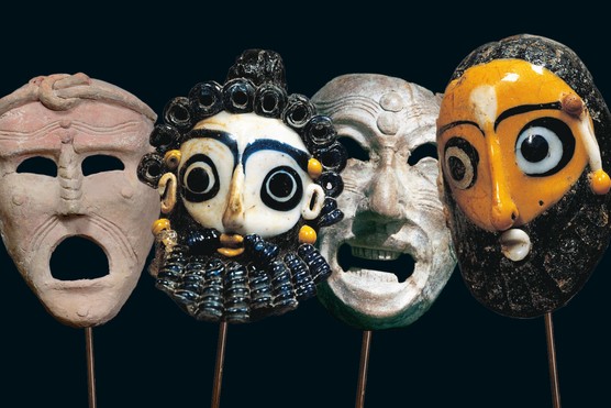 Four small terracotta masks in a line. The two in the middle have black hair and beards, one with a white face and the other with an orange face. The ones on either end are plain beige faces.